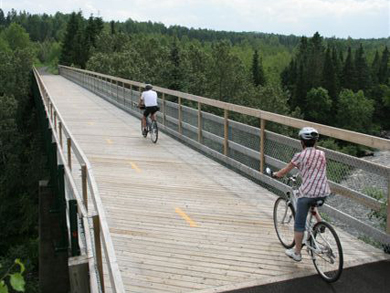 Two cyclists cross over a newly constructed, wooden pedestrian bridge