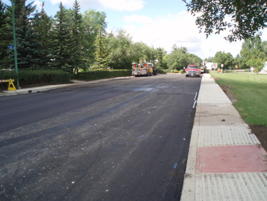 The freshly paved and compacted road surface along Dorothy Street, with new sidewalks and curbs along both sides of the road