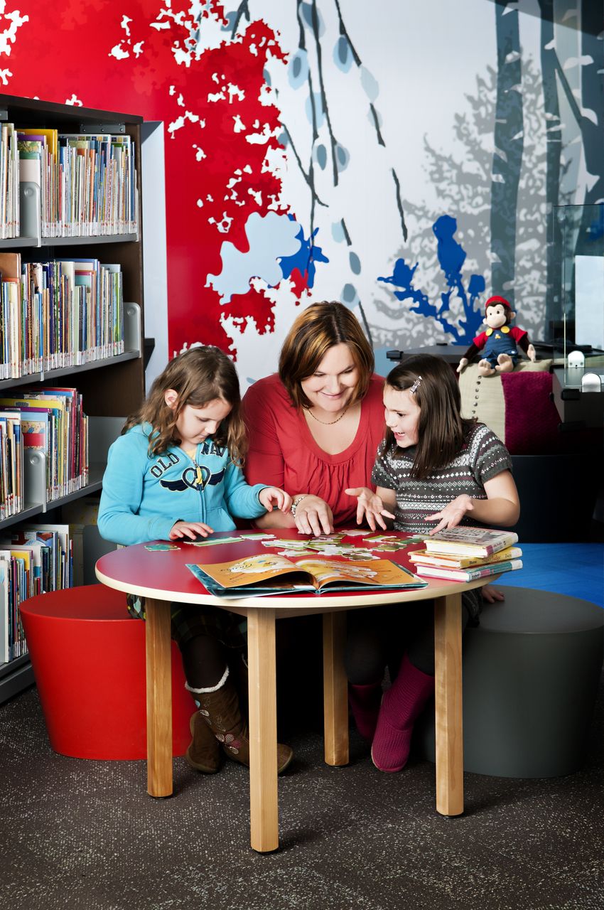 Children and women reading a book at the library