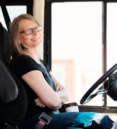 A female bus driver sitting on a bus smiling.