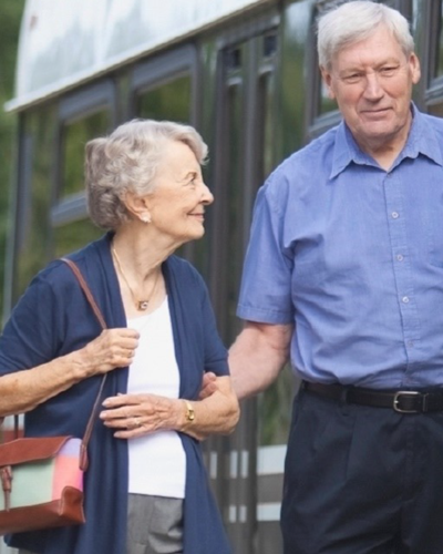 Two seniors, a man and a woman, walk toward a public transit bus.