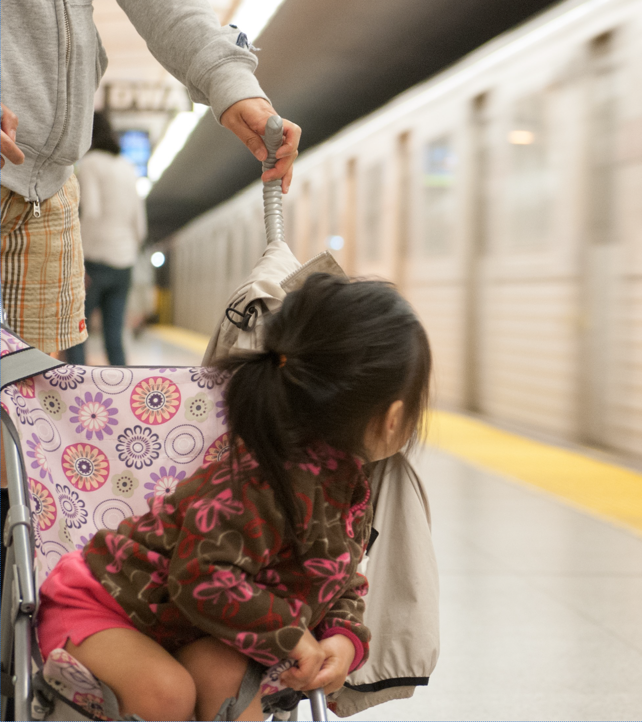 A young girl is pushed in a stroller on a subway platform while a train passes by.