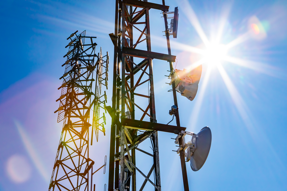 Bright sun shine over two cell site towers, radio and GPS transmitter and receiver
