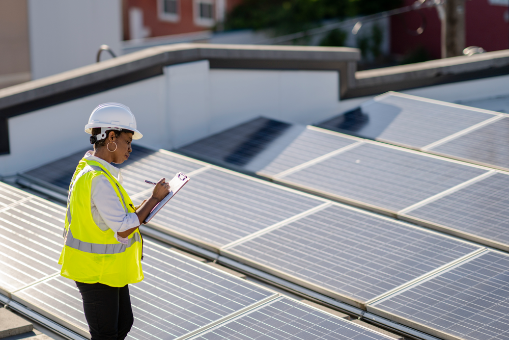 Woman inspecting a rooftop of solar panels while wearing a hard hat and reflective vest